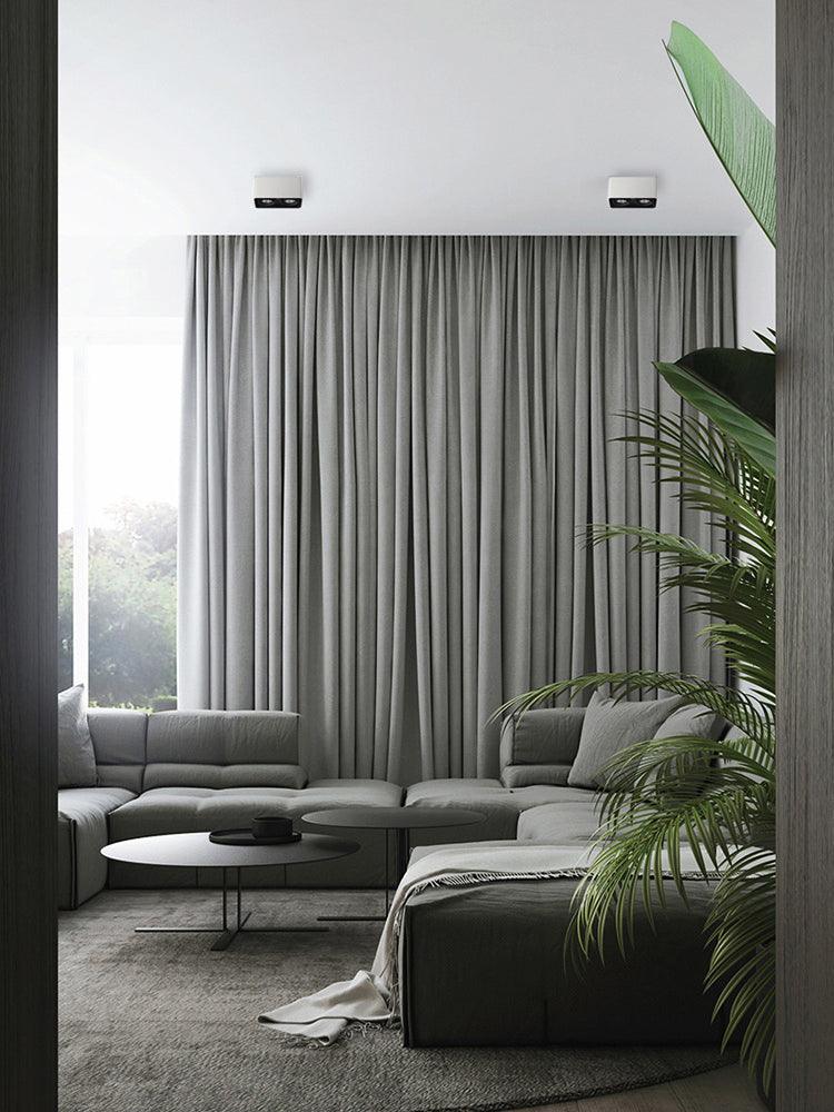Viewed through a doorway, two white single-light Clérachic spotlights sit unlit above a sectional sofa.