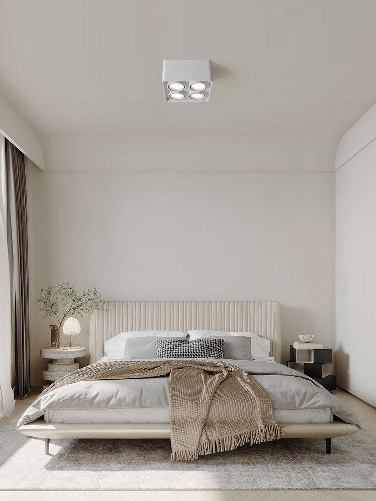 Above a neatly made bed, a white two-light Clérachic spotlight sits unlit on the ceiling.