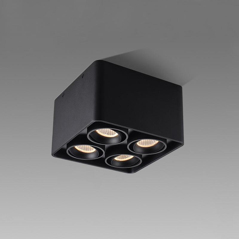 Angled from below-left, this black four-light Clérachic spotlight glows warm against a plain white background.