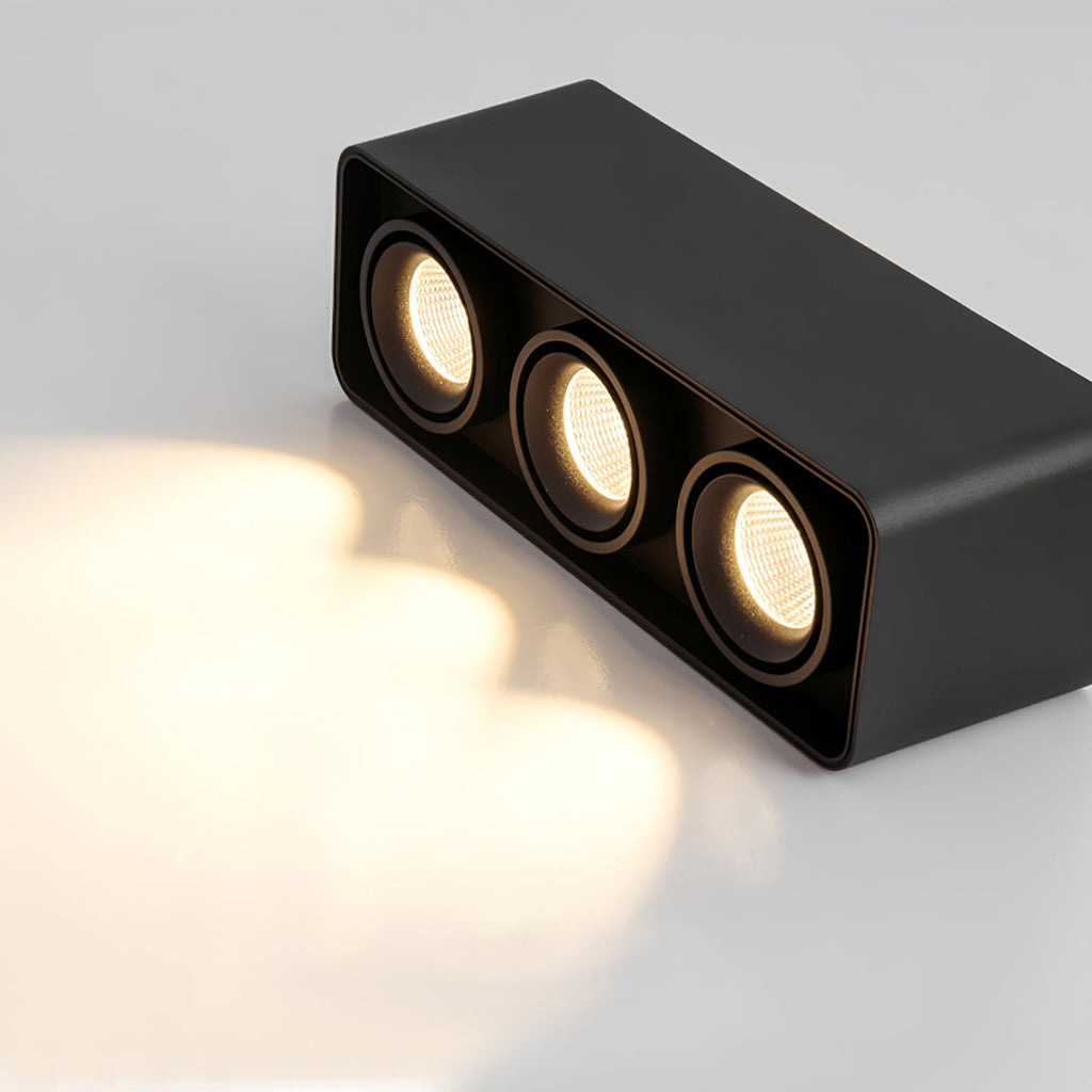 Angled against a dark background, this black three-light Clérachic spotlight casts a visible warm glow from its heads.
