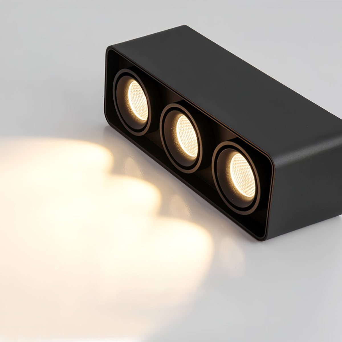 Angled against a dark background, this black three-light Clérachic spotlight casts a visible warm glow from its heads.