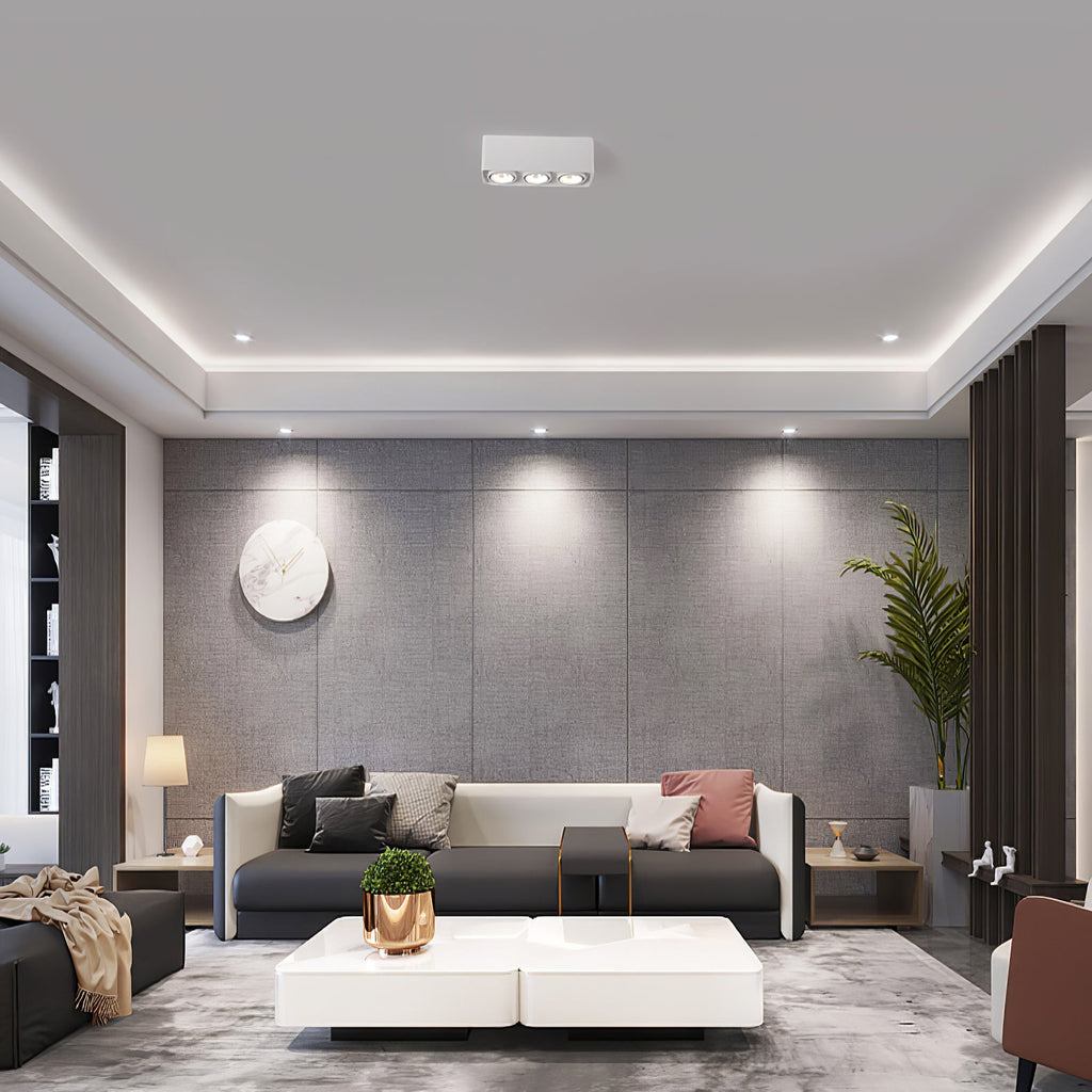 Alongside recessed downlights, a white three-light Clérachic spotlight glows warm above a grey sofa.