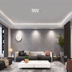 Alongside recessed downlights, a white three-light Clérachic spotlight glows warm above a grey sofa.