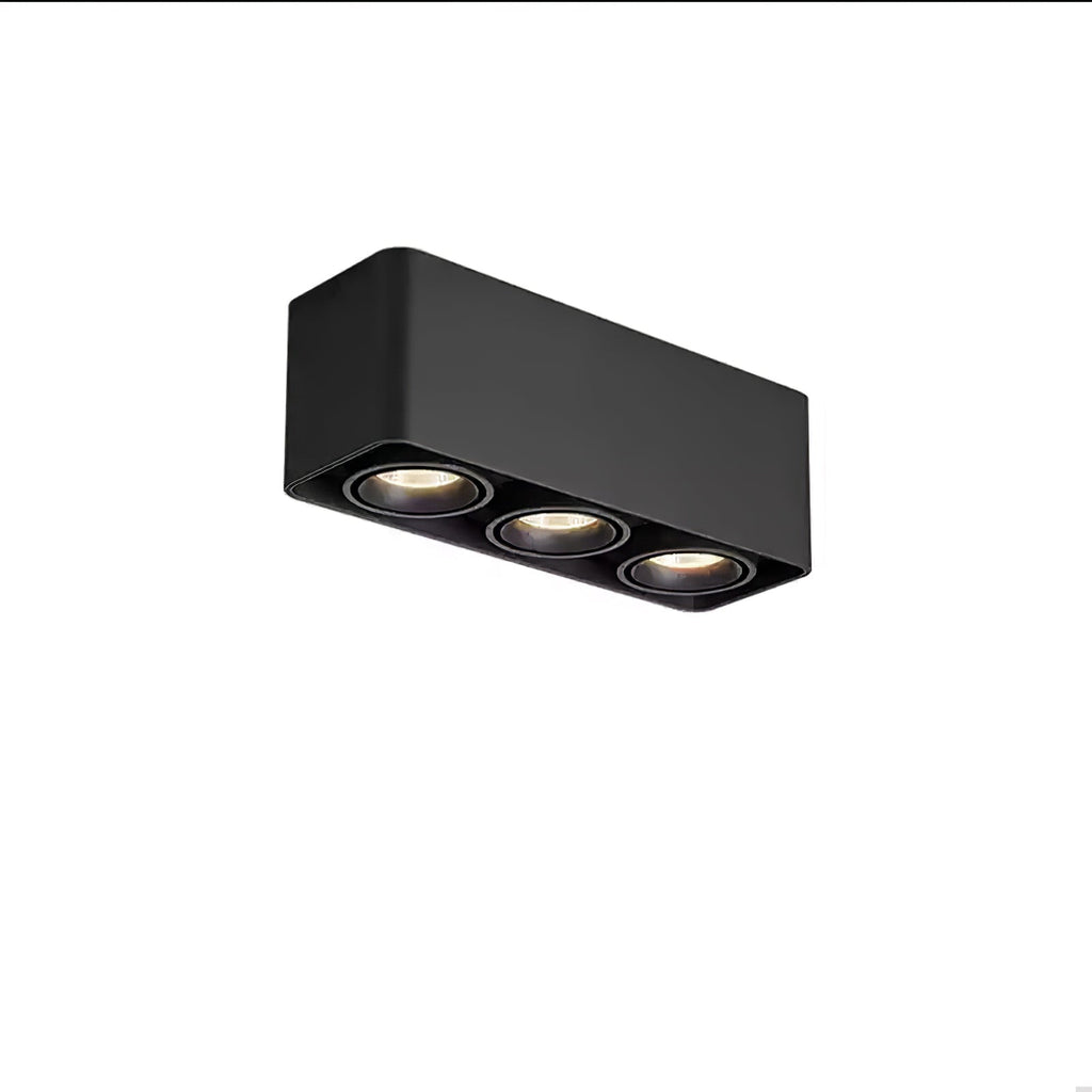 This black three-light Clérachic spotlight glows warm from its three heads, angled on a plain background.