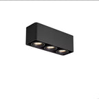 This black three-light Clérachic spotlight glows warm from its three heads, angled on a plain background.