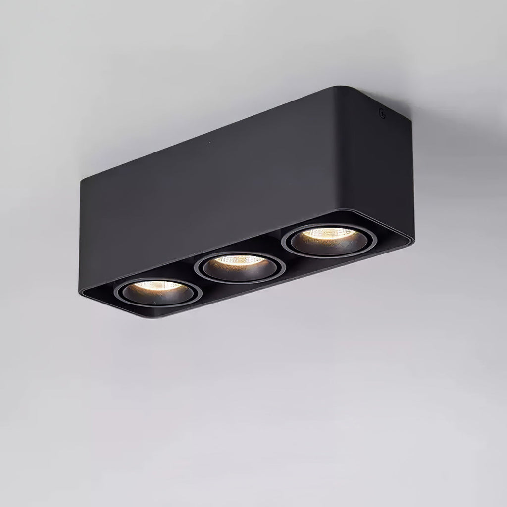 This black three-light Clérachic spotlight glows warm from all three heads against a plain grey background.