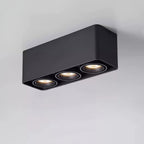 This black three-light Clérachic spotlight glows warm from all three heads against a plain grey background.