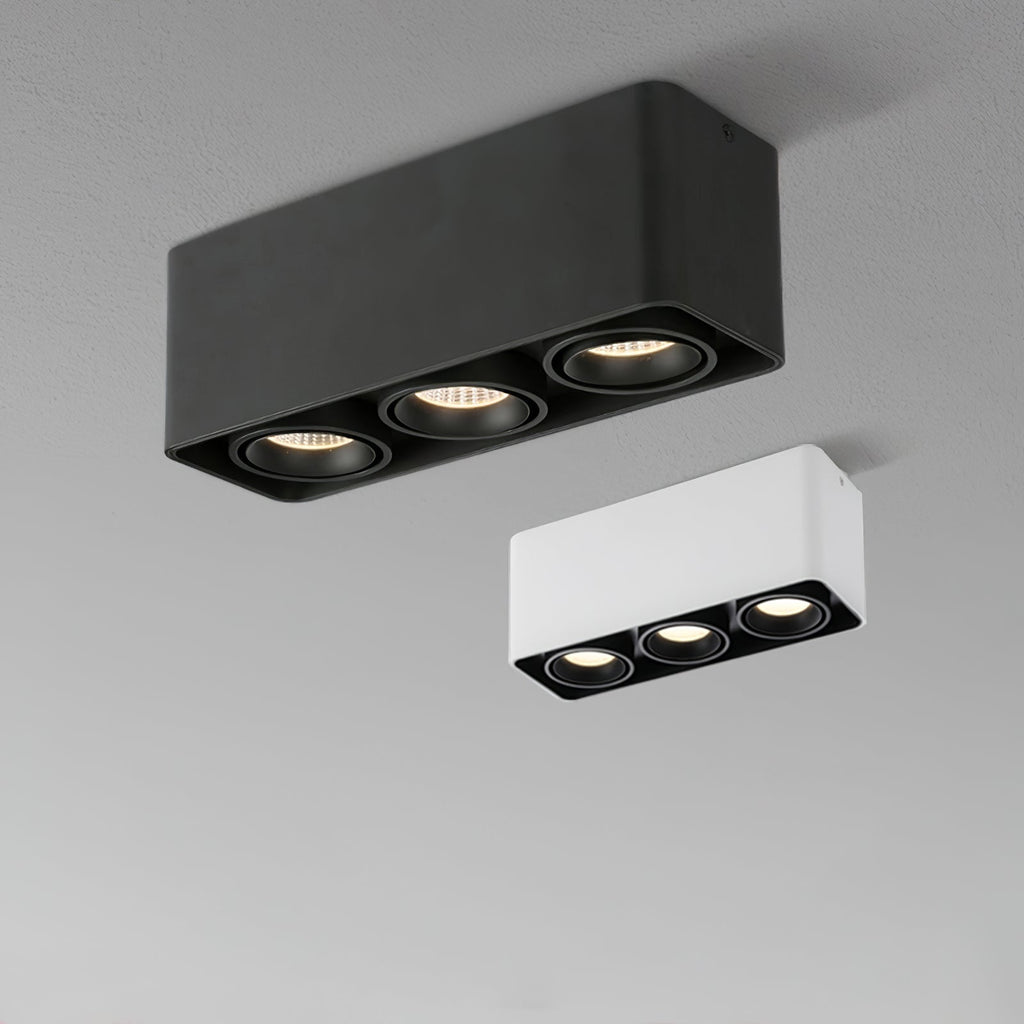 A black three-light Clérachic spotlight glows warm beside its unlit white counterpart on a plain background.