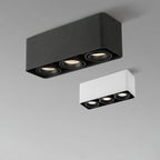 A black three-light Clérachic spotlight glows warm beside its unlit white counterpart on a plain background.