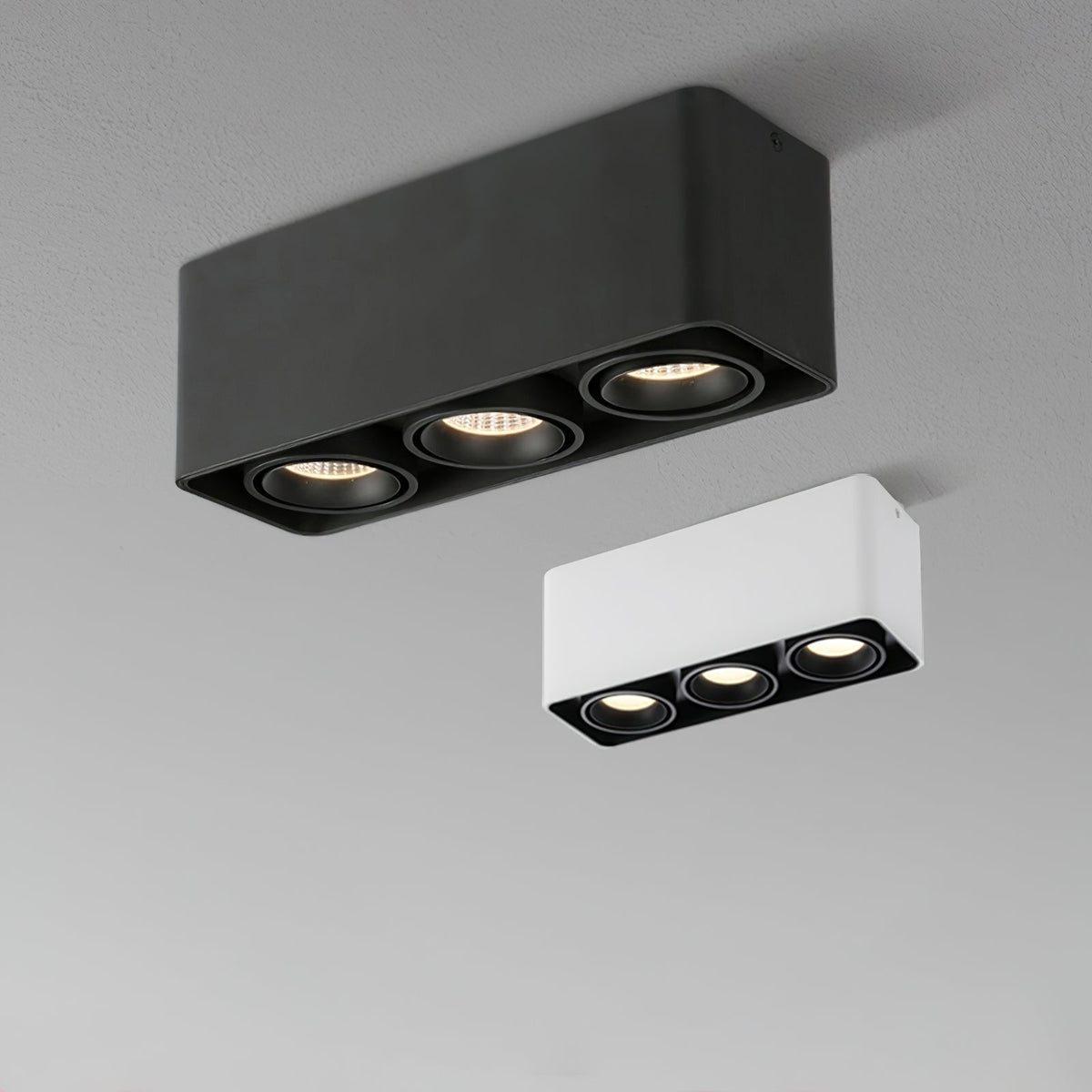 A black three-light Clérachic spotlight glows warm beside its unlit white counterpart on a plain background.