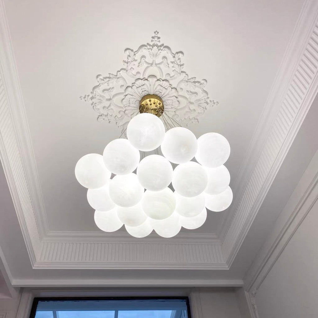 Beneath an ornate ceiling medallion, this Clérachic cluster chandelier hangs unlit, a bright window visible behind it.