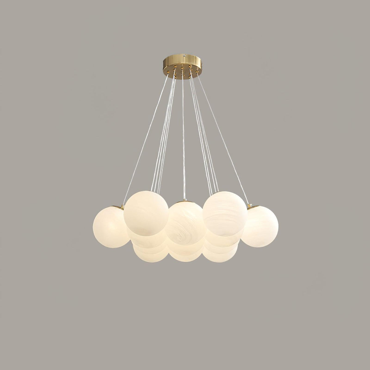 Lit warmly on a grey backdrop, this Clérachic cluster chandelier's frosted globes glow beneath a gold ceiling plate.