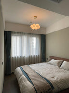 Above a bed dressed in pale linens, this Clérachic cluster chandelier glows softly, sheer curtains at the window.