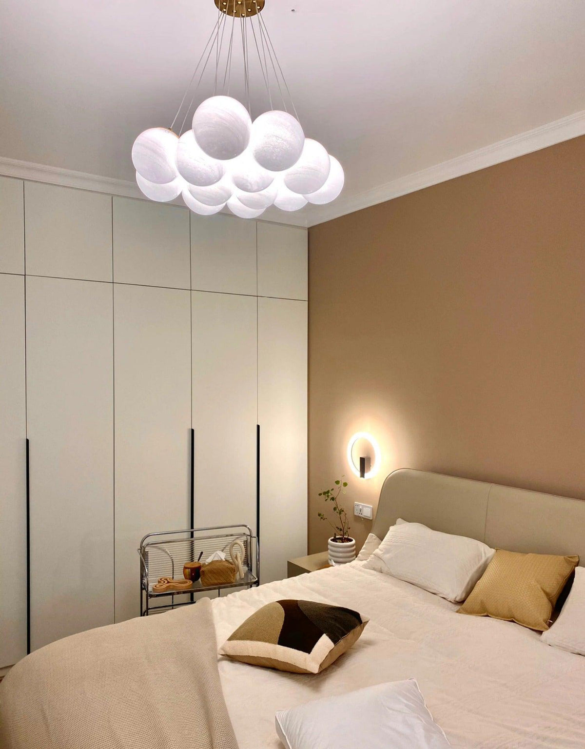 Beside a wall sconce and built-in wardrobe, this Clérachic cluster chandelier hangs unlit in a bedroom.