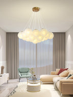 A green armchair and pale sofa sit beneath this lit Clérachic cluster chandelier in a neutral living room.