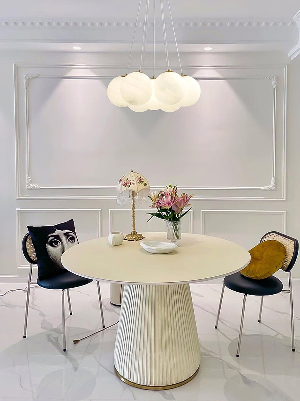 Above a round dining table with black chairs, this Clérachic cluster chandelier hangs lit in a panelled room.