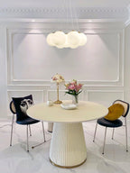 Above a round dining table with black chairs, this Clérachic cluster chandelier hangs lit in a panelled room.