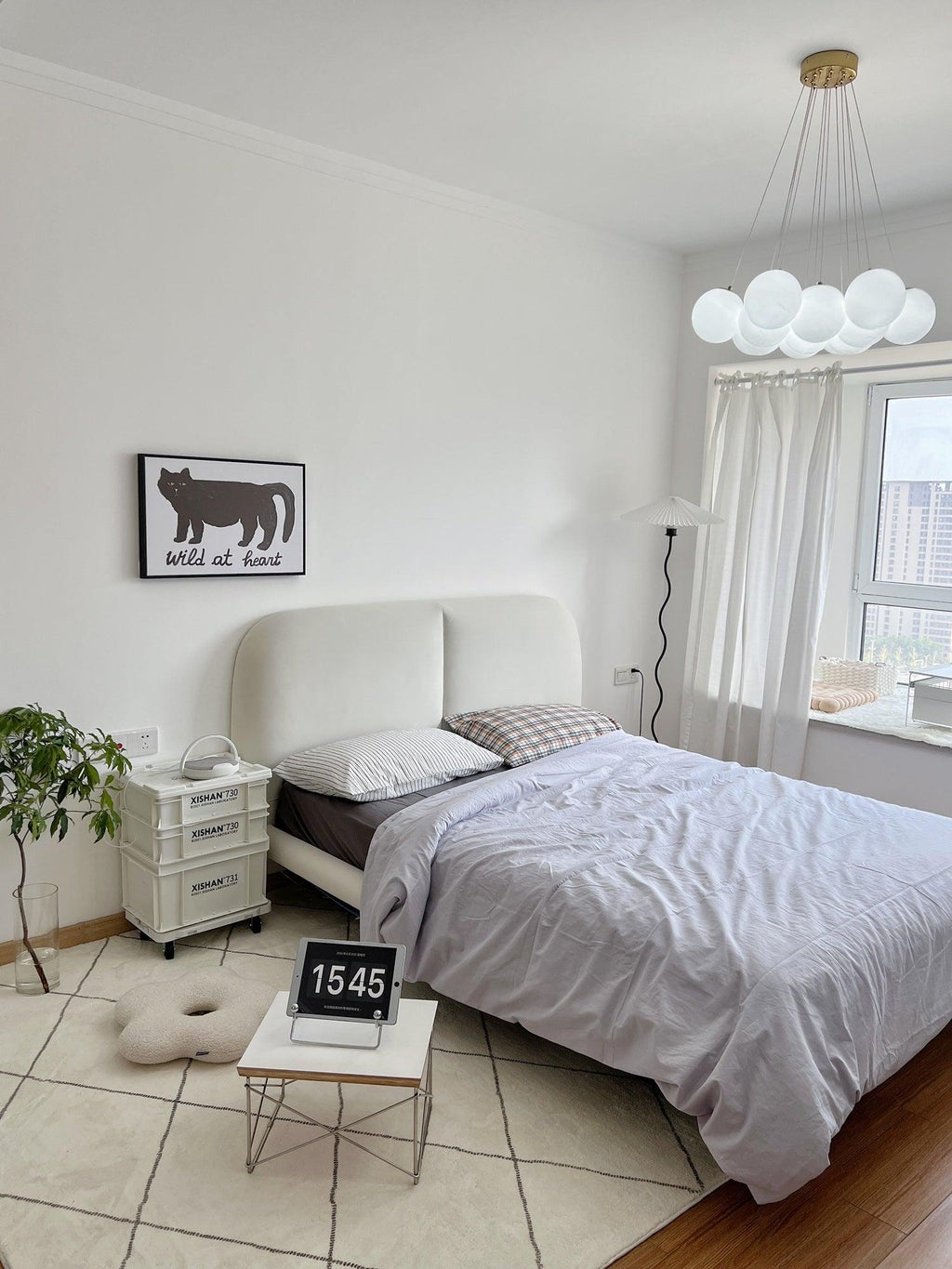 A framed print hangs on the wall beneath this lit Clérachic cluster chandelier above grey bedding.