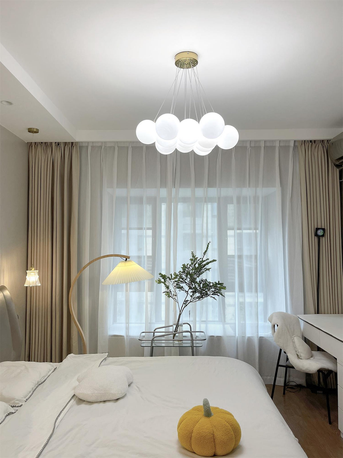 White bedding and a floor lamp sit beneath this lit Clérachic cluster chandelier, sheer curtains softening the light.
