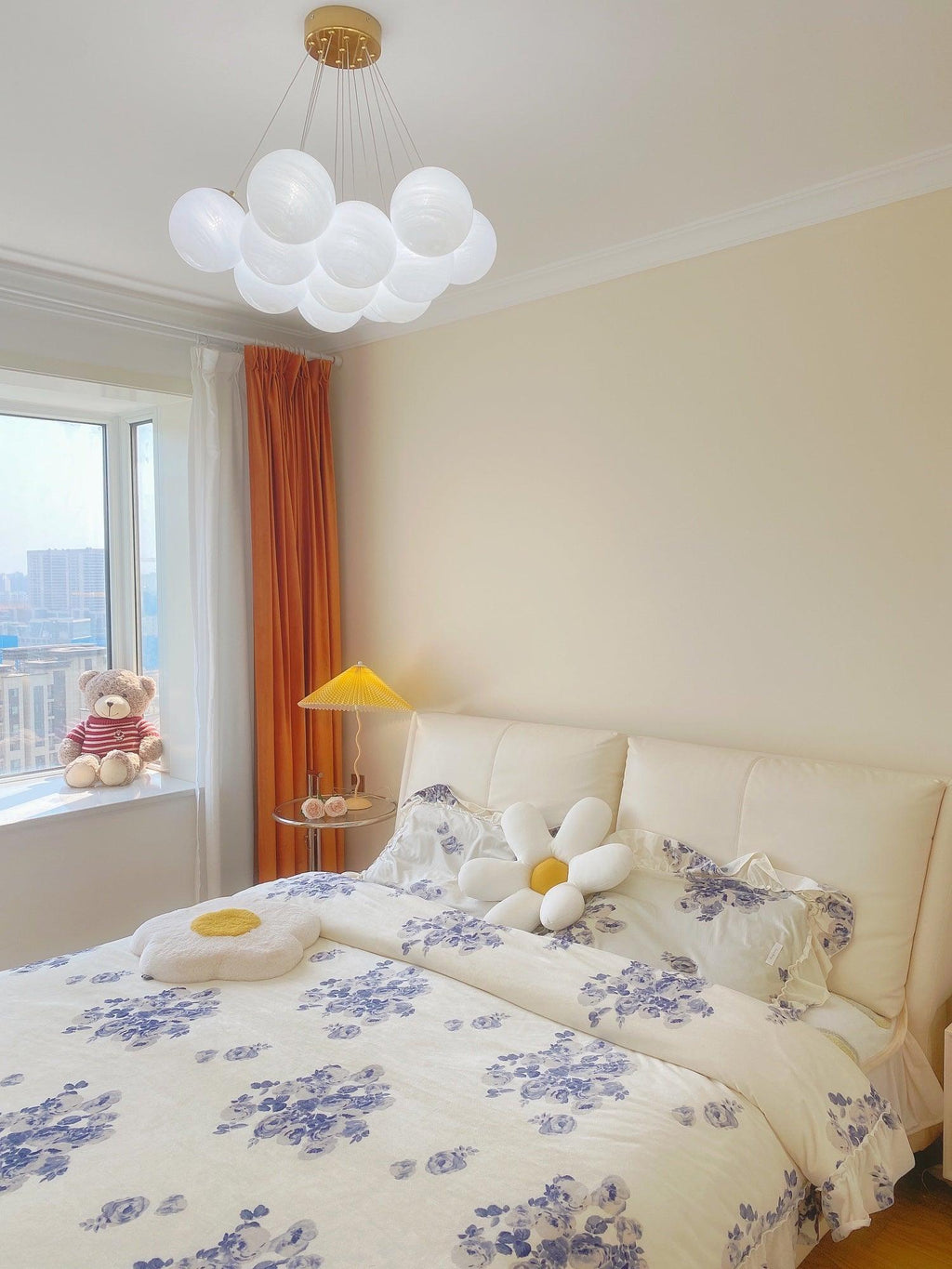 A closer view shows this unlit Clérachic cluster chandelier above the same floral-bedded bed and orange curtains.