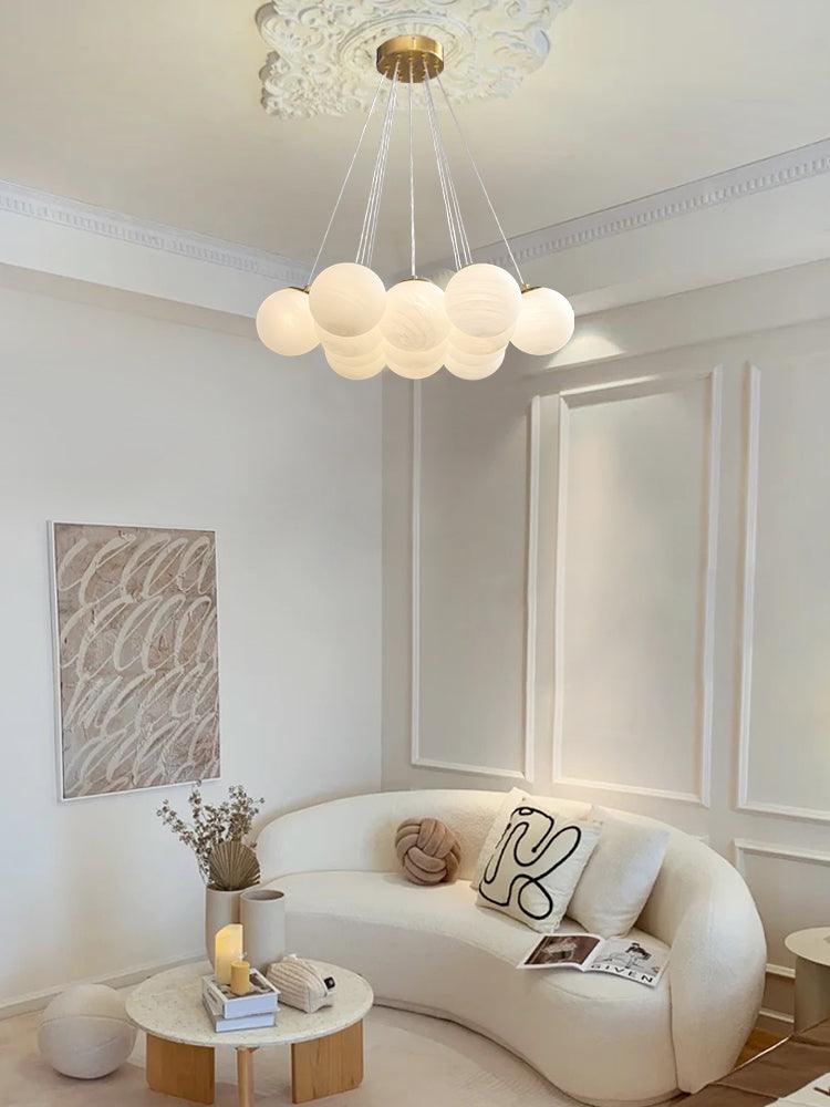 A curved white sofa and a textured wall print sit beneath this lit Clérachic cluster chandelier.