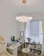 A desk and open shelving sit beneath this lit Clérachic cluster chandelier in a home study corner.