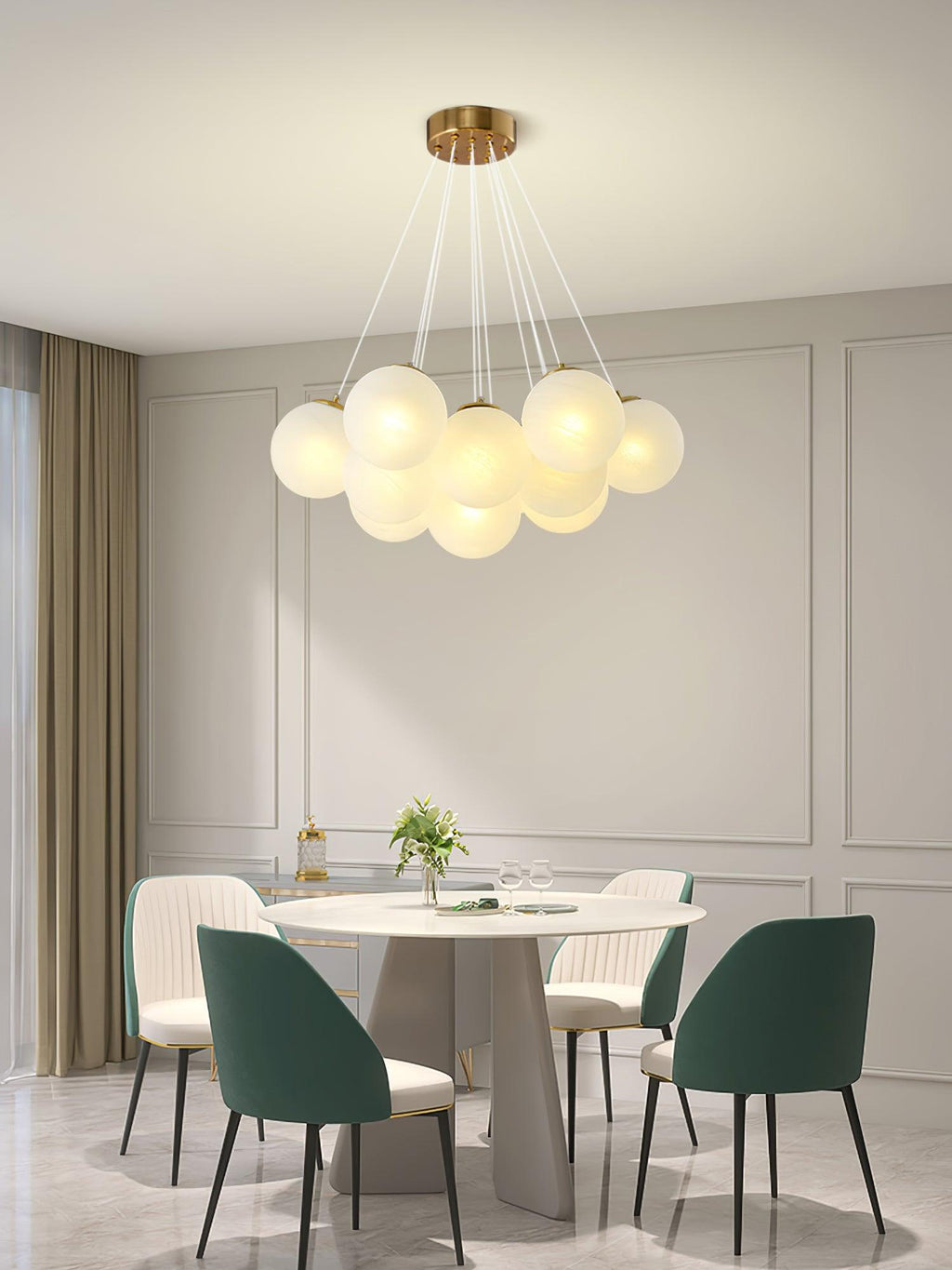 Green upholstered chairs surround a round dining table beneath this lit Clérachic cluster chandelier in a panelled room.
