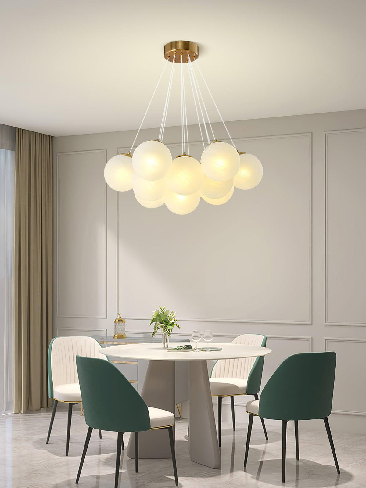 Green upholstered chairs surround a round dining table beneath this lit Clérachic cluster chandelier in a panelled room.