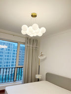 A window overlooking the city sits beside this lit Clérachic cluster chandelier above a grey-dressed bed.