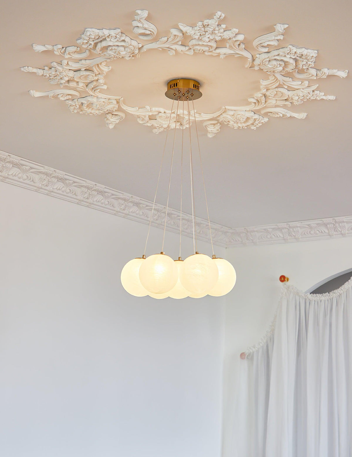 Close view of the gold ceiling plate on this lit Clérachic cluster chandelier, set within an ornate plaster ceiling rose.