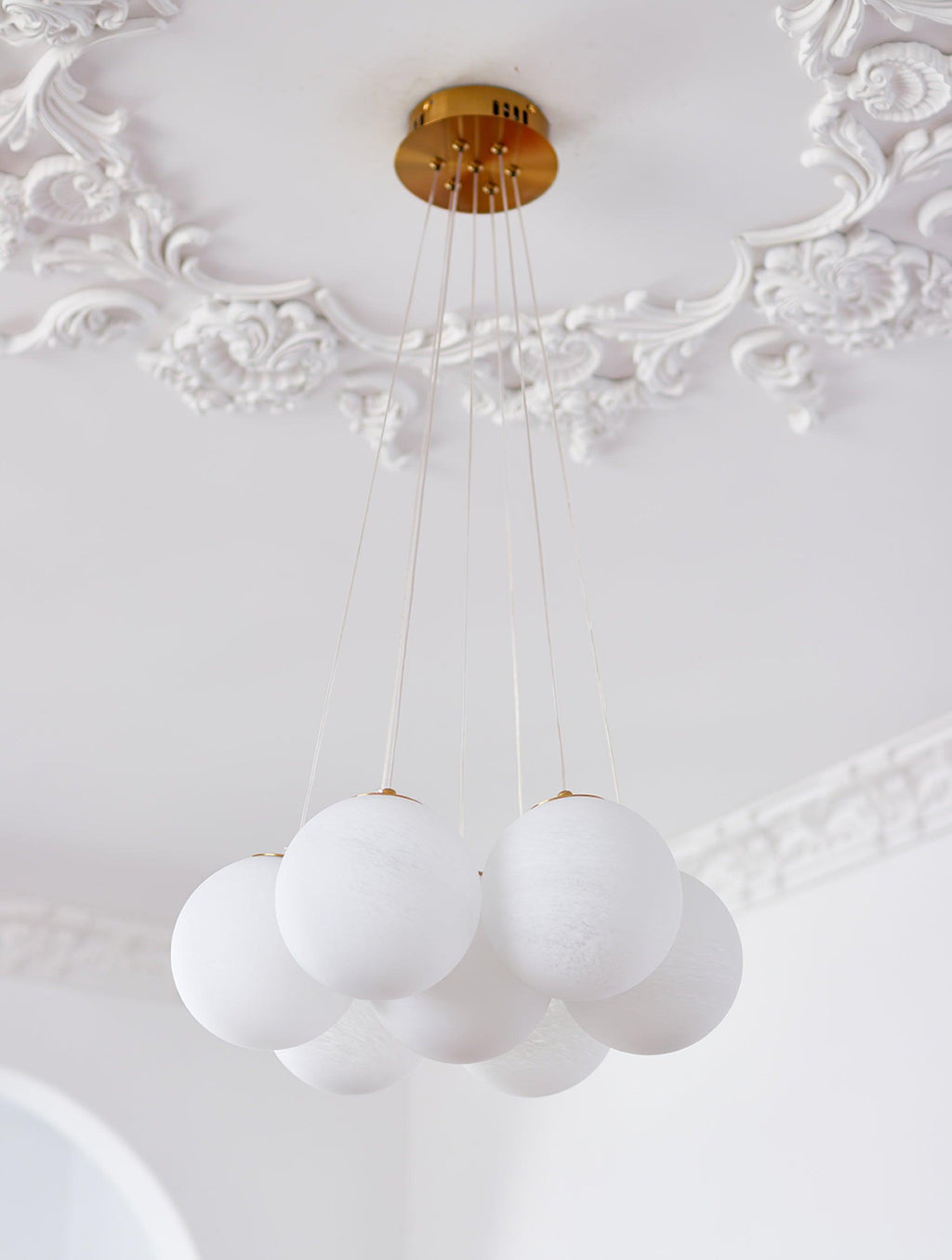 Cords descend from the gold ceiling plate of this unlit Clérachic cluster chandelier beneath ornate ceiling moulding.