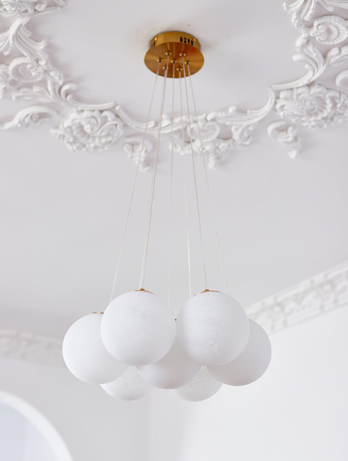 Cords descend from the gold ceiling plate of this unlit Clérachic cluster chandelier beneath ornate ceiling moulding.