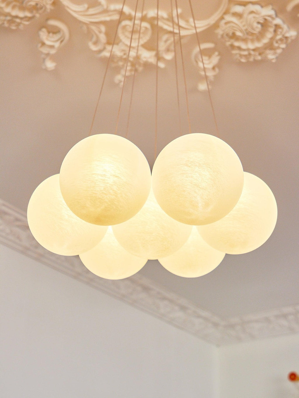 Lit and viewed from below, the frosted glass globes of this Clérachic cluster chandelier glow warmly beneath ornate moulding.