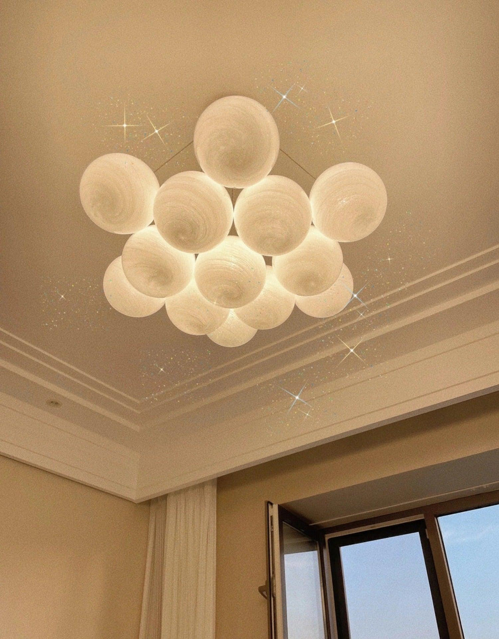 This unlit Clérachic cluster chandelier is shown close, with light flares added around its frosted globes near a ceiling corner.