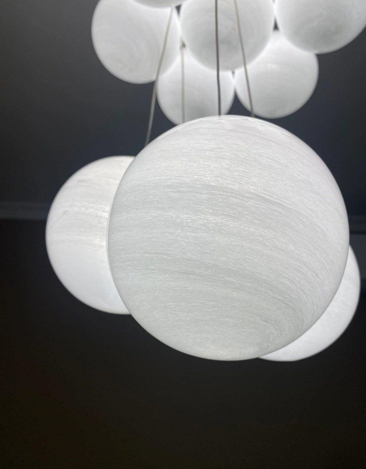 Extremely close, the swirled texture of this Clérachic cluster chandelier's frosted globes glows against a dark background.