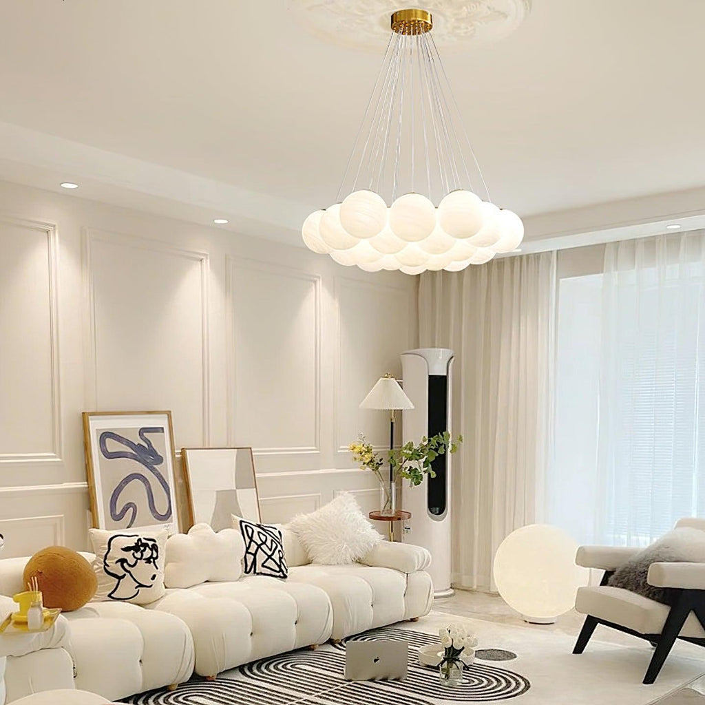 In a cream living room with ornate wall panelling, this Clérachic cluster chandelier hangs unlit above a patterned rug and framed art.
