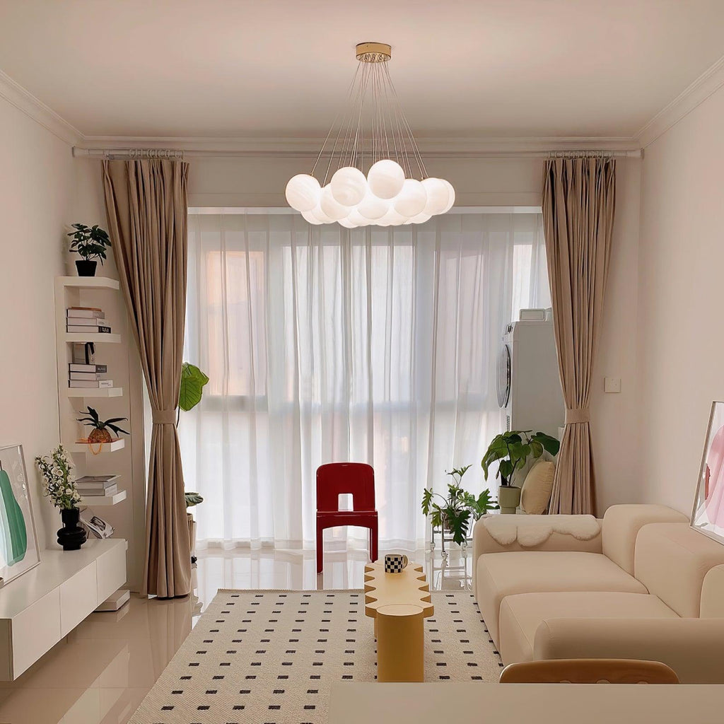 Sheer curtains and a red accent chair frame this lit Clérachic cluster chandelier in a bright living room.
