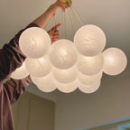 A hand holds the frosted glass globes of this Clérachic cluster chandelier, their swirled texture visible up close.