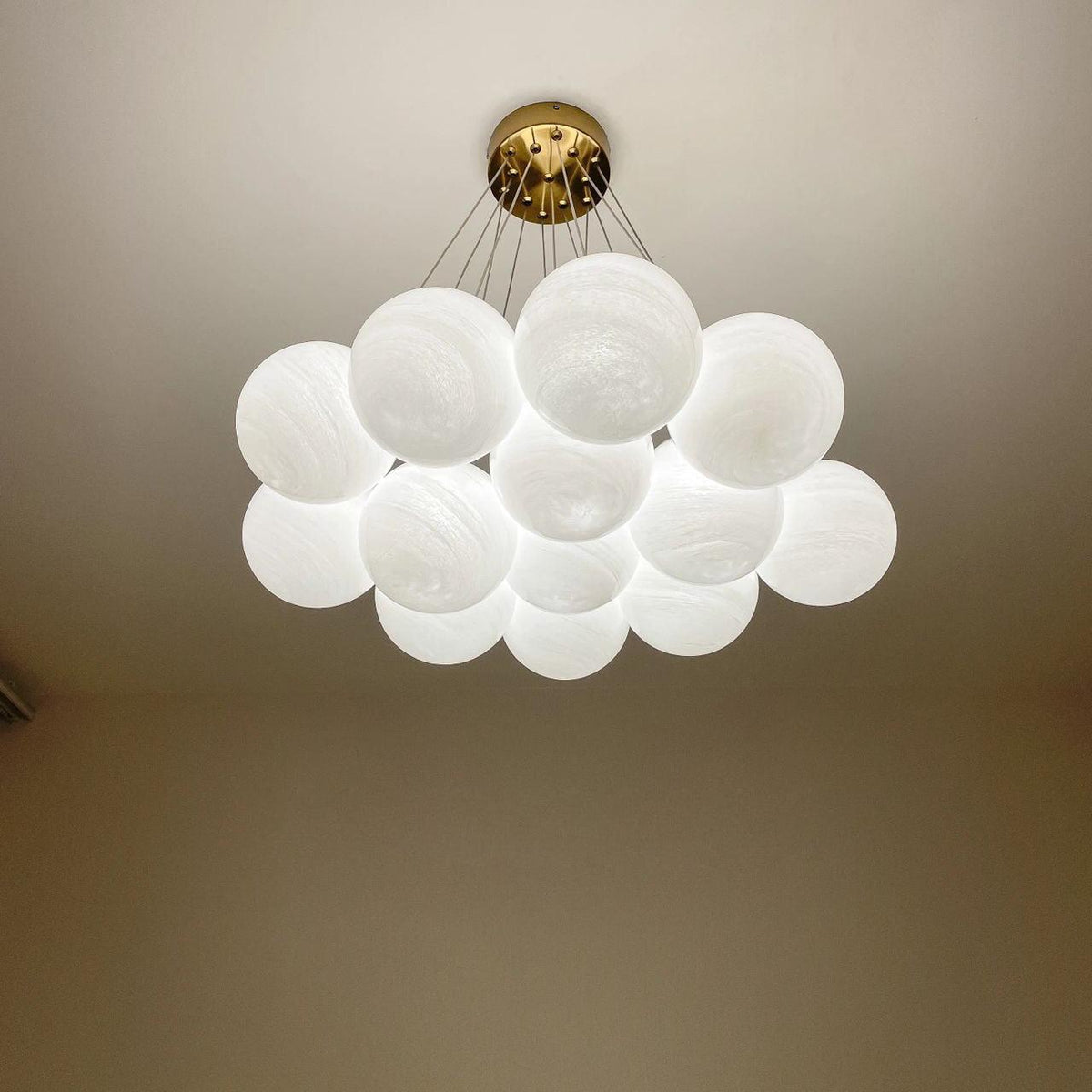 Seen close against the ceiling, this lit Clérachic cluster chandelier shows its gold mounting plate against a warm brown wall.