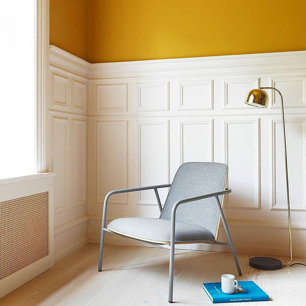 Gold dome-shade floor lamp from Clérachic beside a grey armchair in a room with mustard-yellow upper walls.