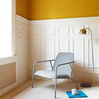 Gold dome-shade floor lamp from Clérachic beside a grey armchair in a room with mustard-yellow upper walls.