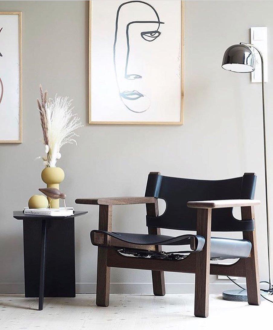 A dark table with framed line art sits near this gold dome-shade Clérachic floor lamp and a black leather chair.