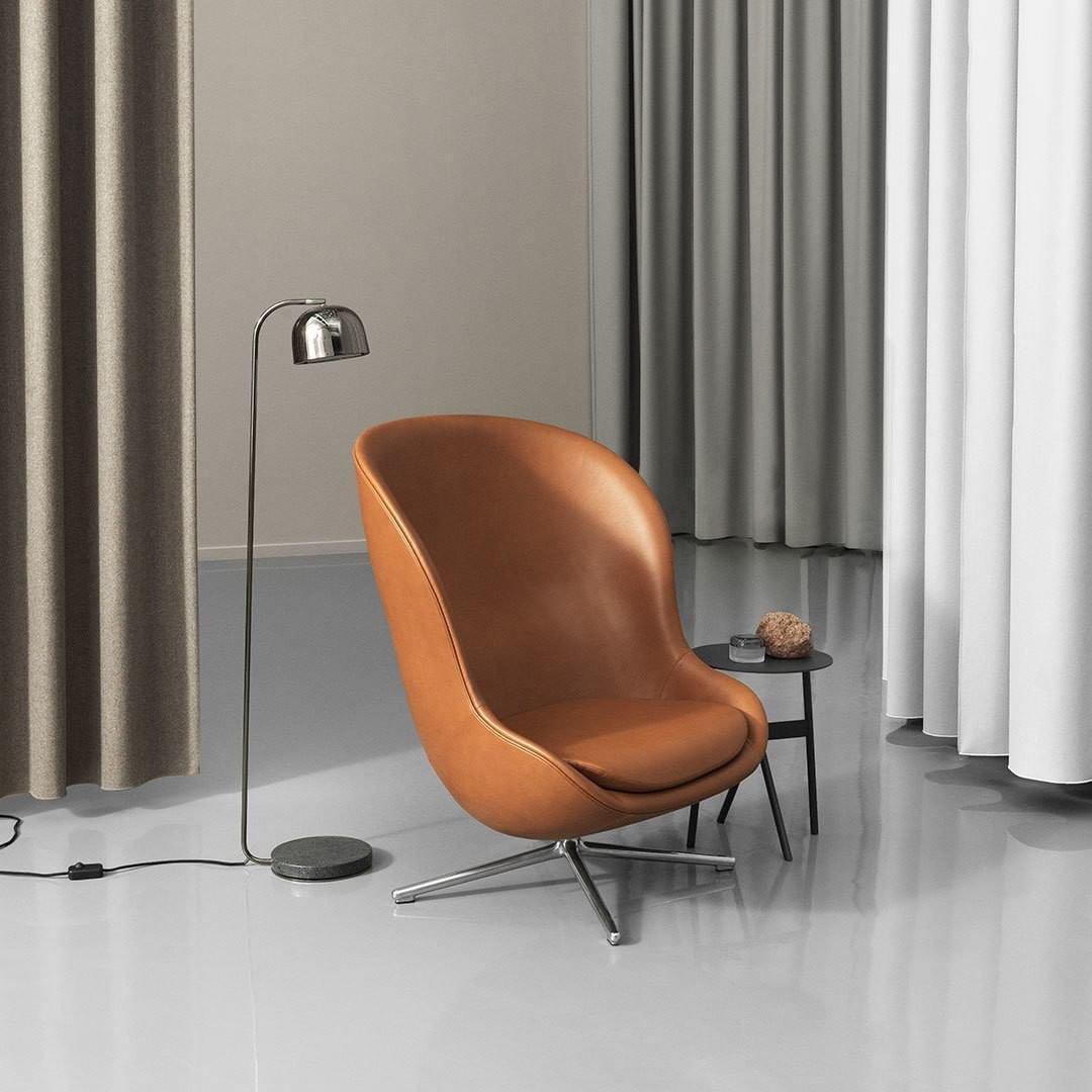 Black dome-shade floor lamp from Clérachic standing next to a tan leather armchair against sheer curtains.