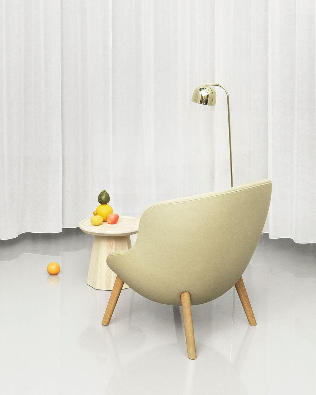 A round side table scattered with fruit sits by this gold dome-shade Clérachic floor lamp and a cream accent chair.