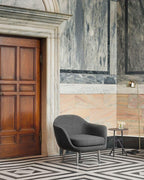 In a marble-panelled hallway, this gold dome-shade Clérachic floor lamp stands beside a wooden door and a chair.