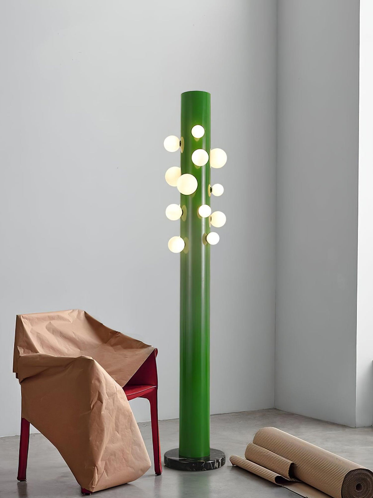 Cropped tighter on the paper-wrapped chair, this green Clérachic floor lamp again lights a concrete-floored staging corner.