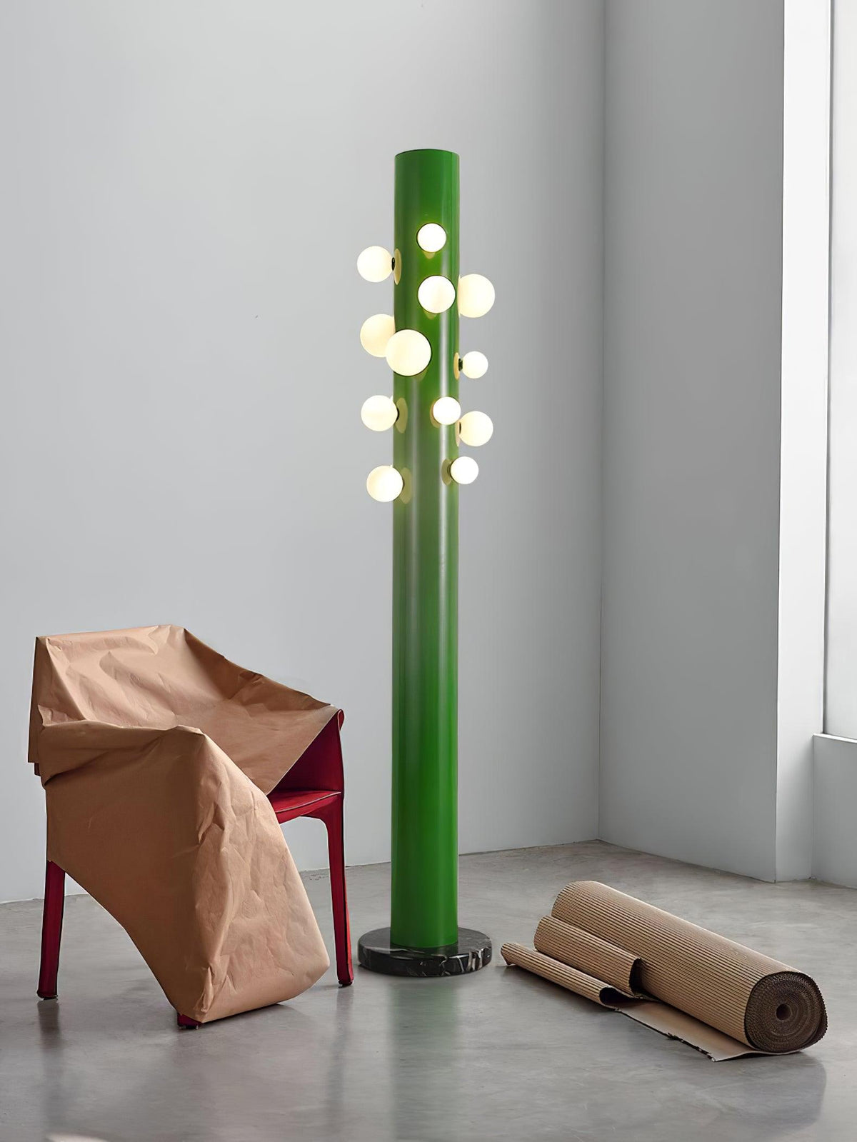 A closer crop shows the green Clérachic floor lamp's base beside the leaning paper-wrapped chair on bare concrete.