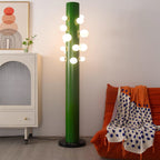 Set closer to camera near the same cream cabinet, the green Clérachic floor lamp's globes cast warm light over the orange throw.