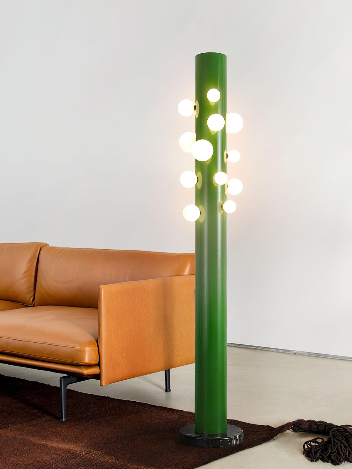 Next to a tan leather sofa and a dark cowhide rug, the green Clérachic floor lamp lights a warm living room corner.