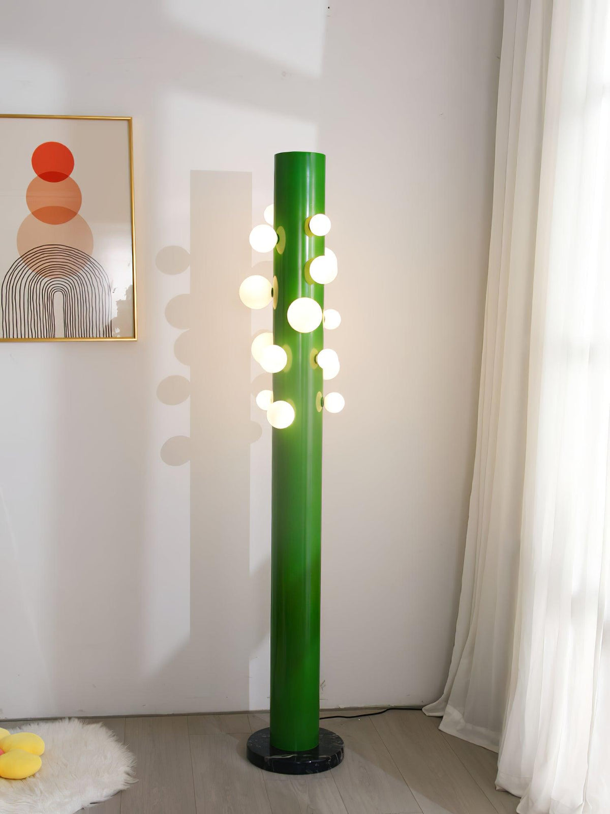 A wider view shows the green Clérachic floor lamp beside the sheer curtain, framed print and sheepskin rug together.